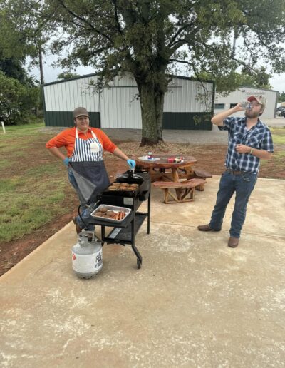 Chef grills hamburgers and hotdogs while party goers enjoy the party.