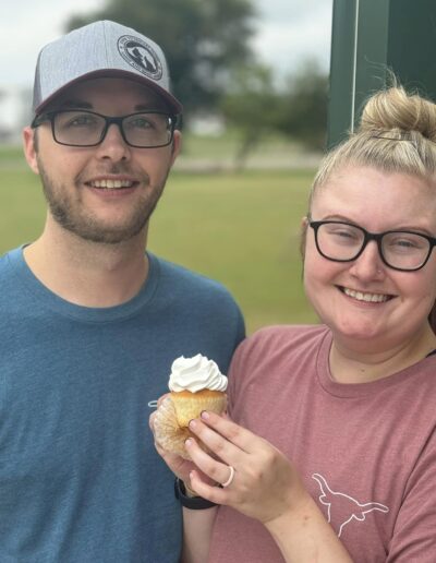 Couple posing for a picture with a cupcake in hand while they smile