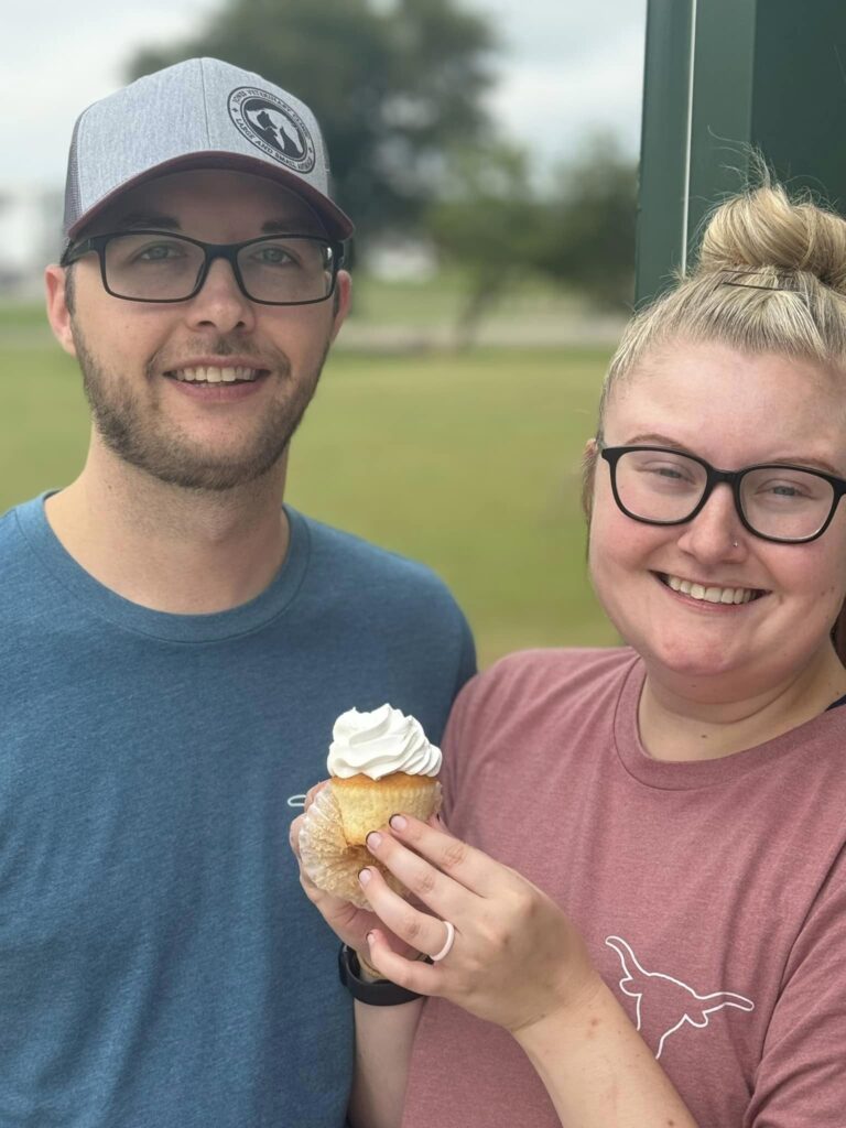 Couple posing for a picture with a cupcake in hand while they smile